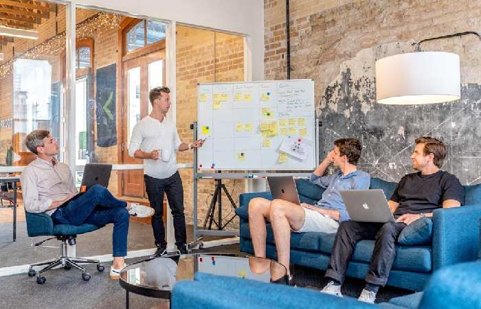 A group of professionals discussing around a table, each with laptops, focused on autonomous decision-making in IoT systems.